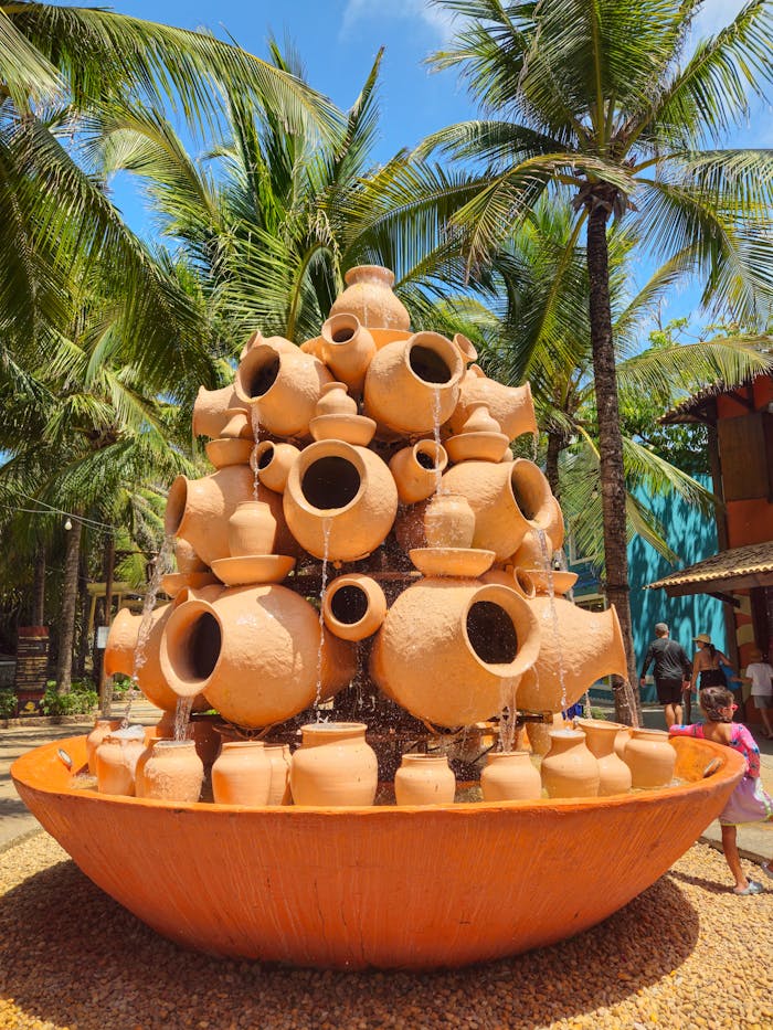 Charming clay pot fountain surrounded by palm trees outdoors, blending art with nature.