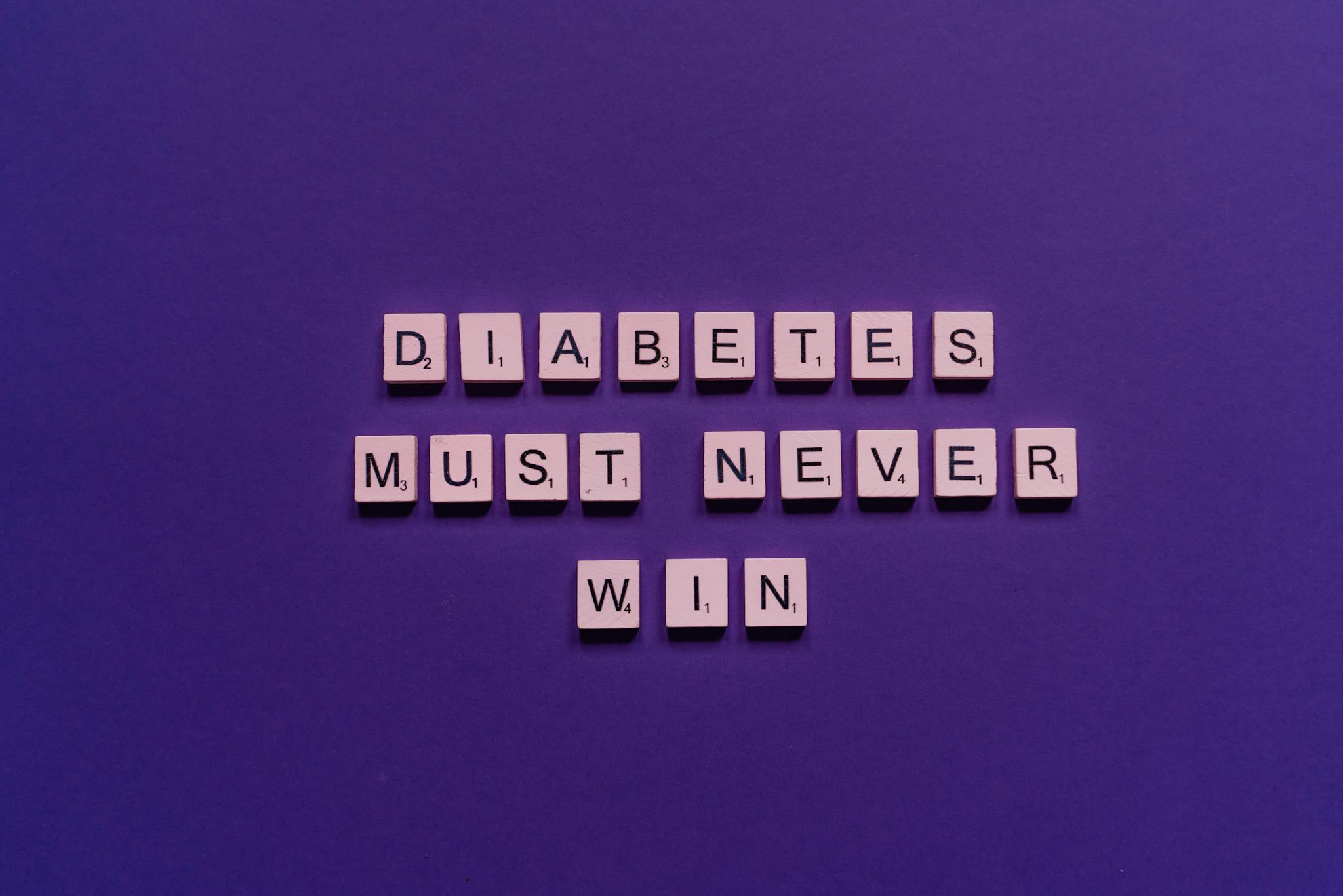 Tile letters on purple background spelling 'Diabetes Must Never Win' for awareness.