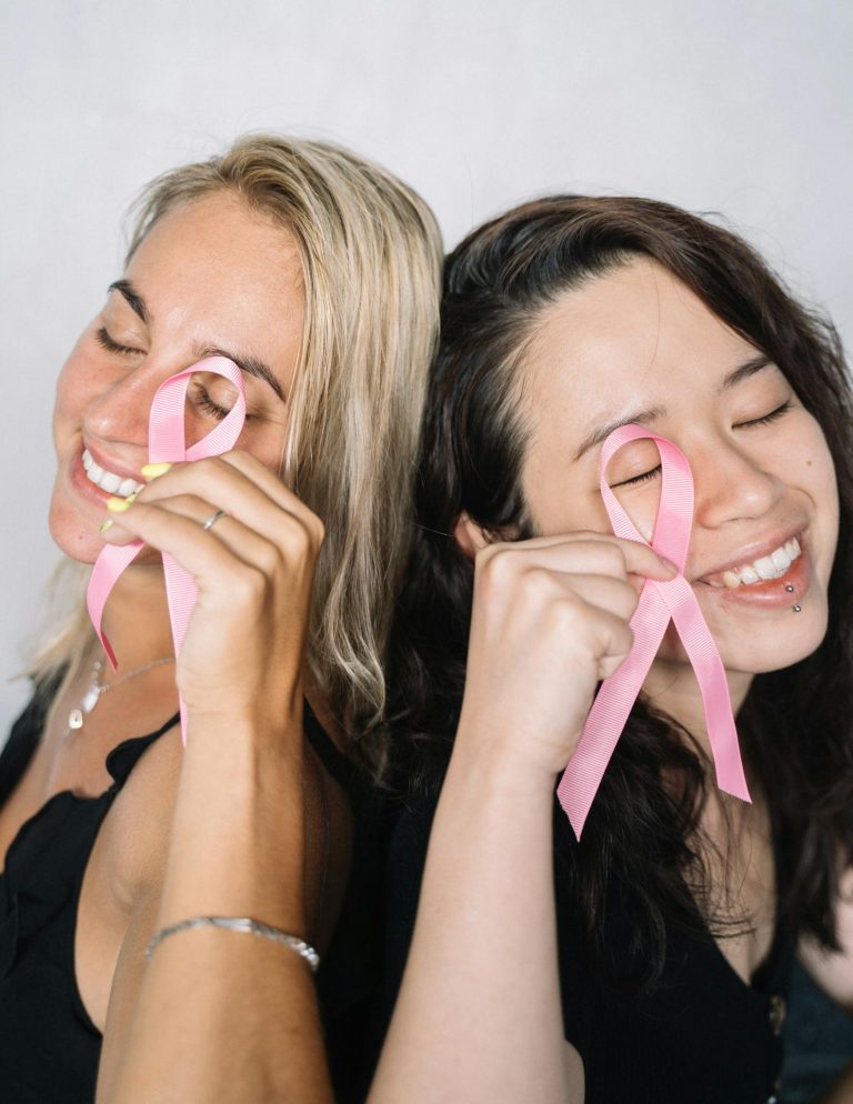 Two women holding pink ribbons, symbolizing breast cancer awareness and solidarity.